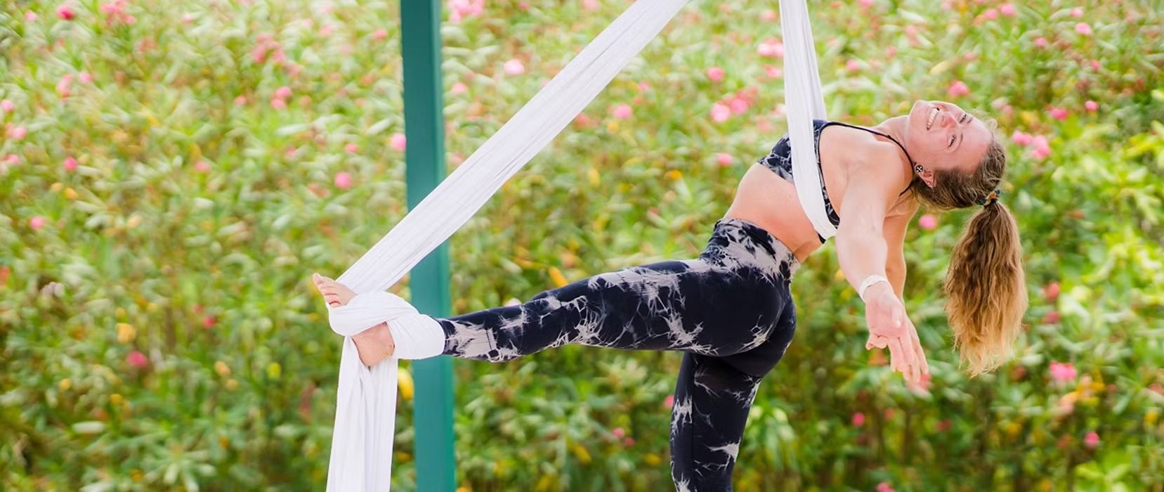 Aerialist smiling in a backbend on white silks in the garden