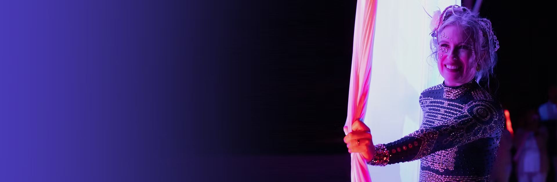 Meredith smiling between pink silks in a sparkling costume