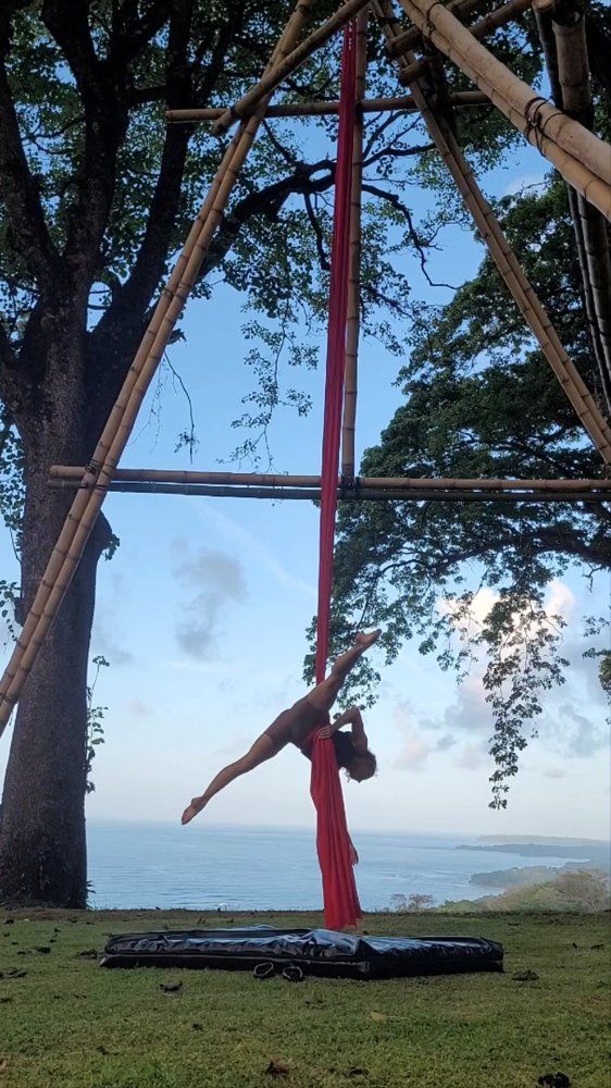 Julia Torggler on red aerial silks overlooking the ocean