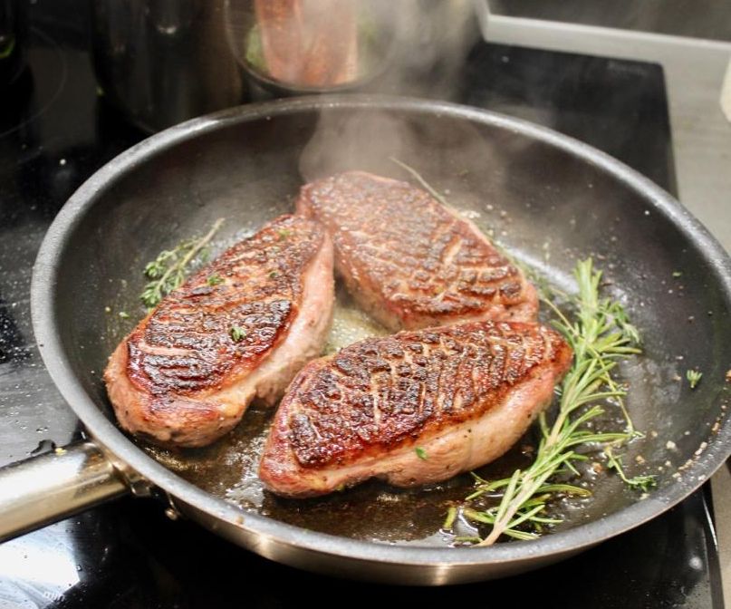 Steaks searing in a pan with rosemary