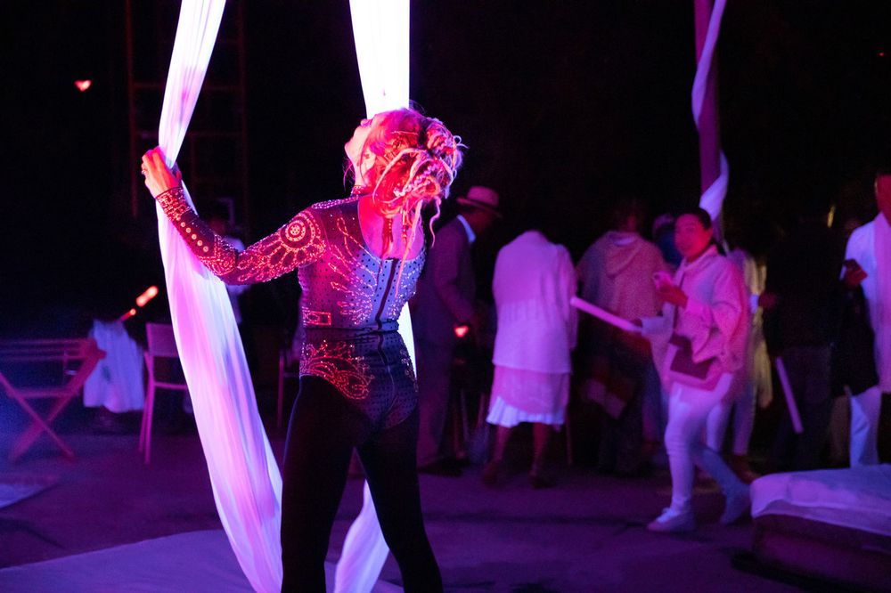 Aerialist in a sequinned costume performing with silks at a night party