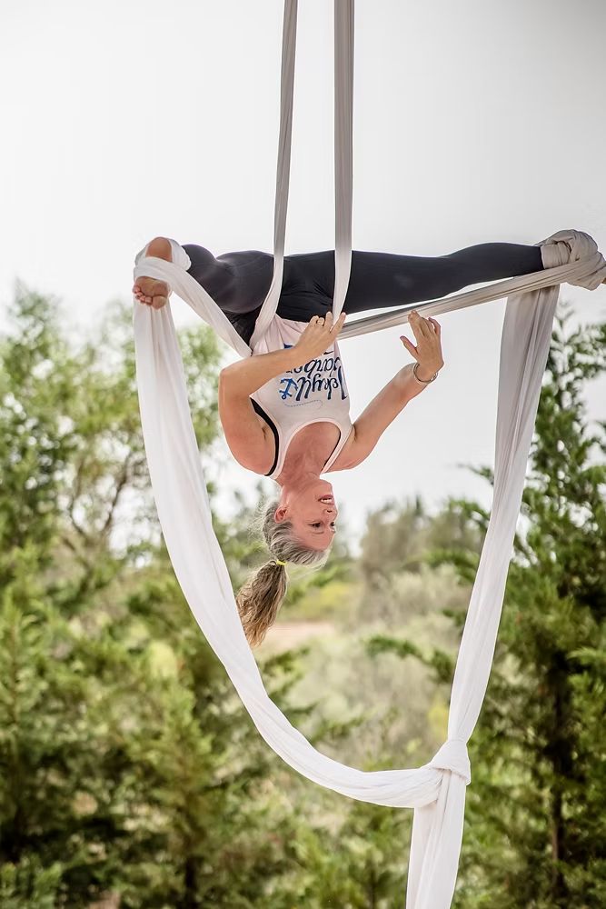 Aerialist hanging upside down in white silks among the trees
