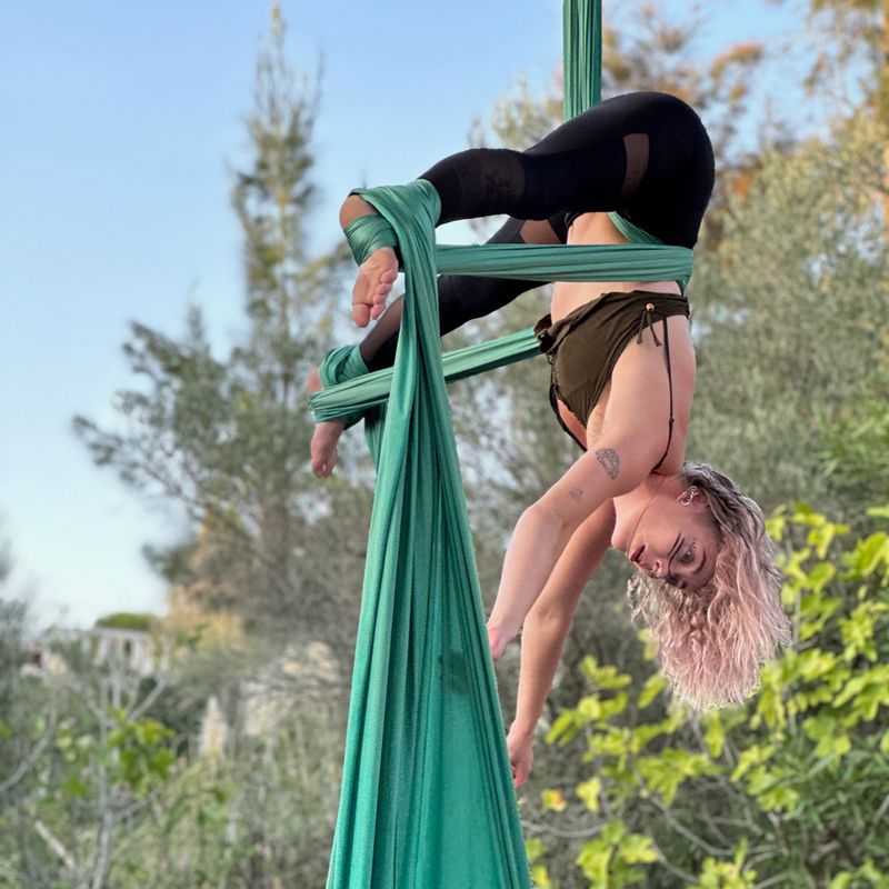 Aerialist inverted in green silks among the trees