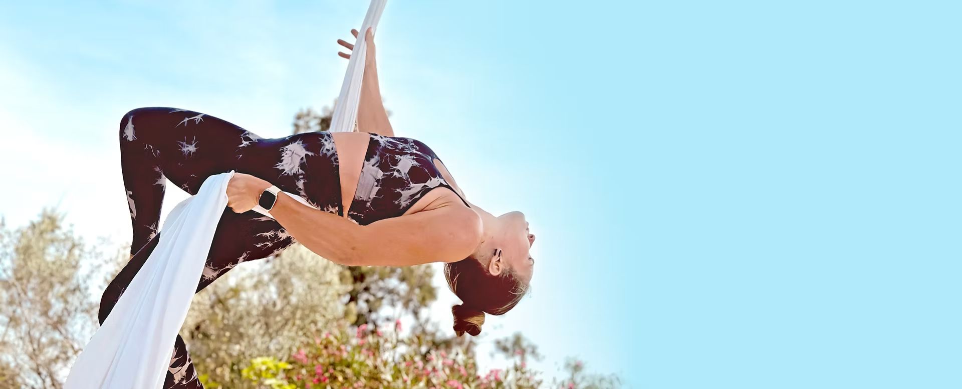 Aerialist arching back from white silks against a blue sky