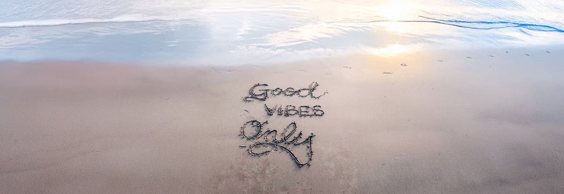 “Good vibes only” written in the sand on a beach